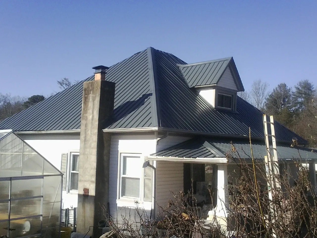 Dark blue standing seam metal roof on a white farmhouse with dormer — Slate & Tile Roof Repair by Roofing Brothers in Park Ridge