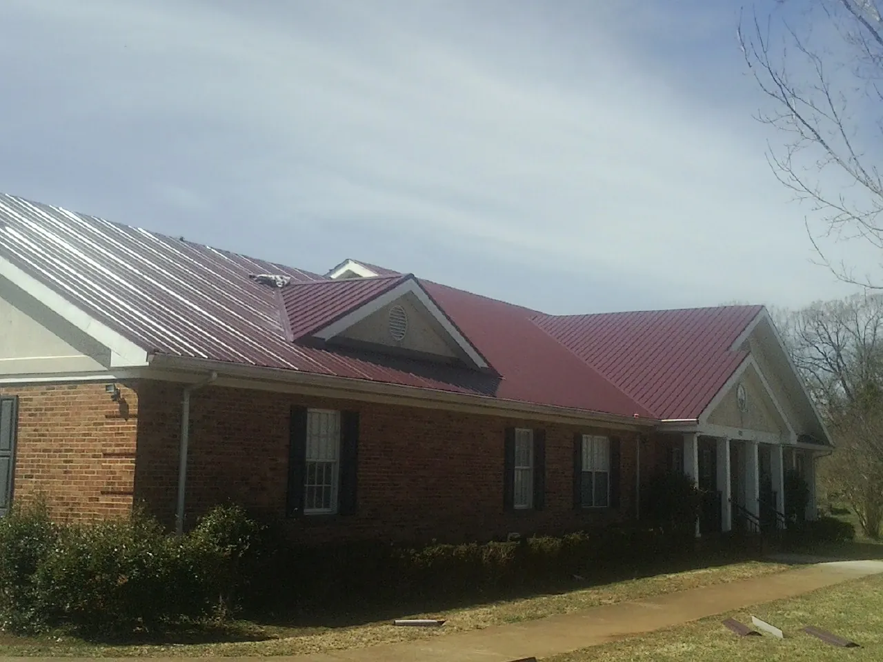 Red metal roof with gabled entries on a long brick building, from a Hail Damage Roof Repair job in Park Ridge