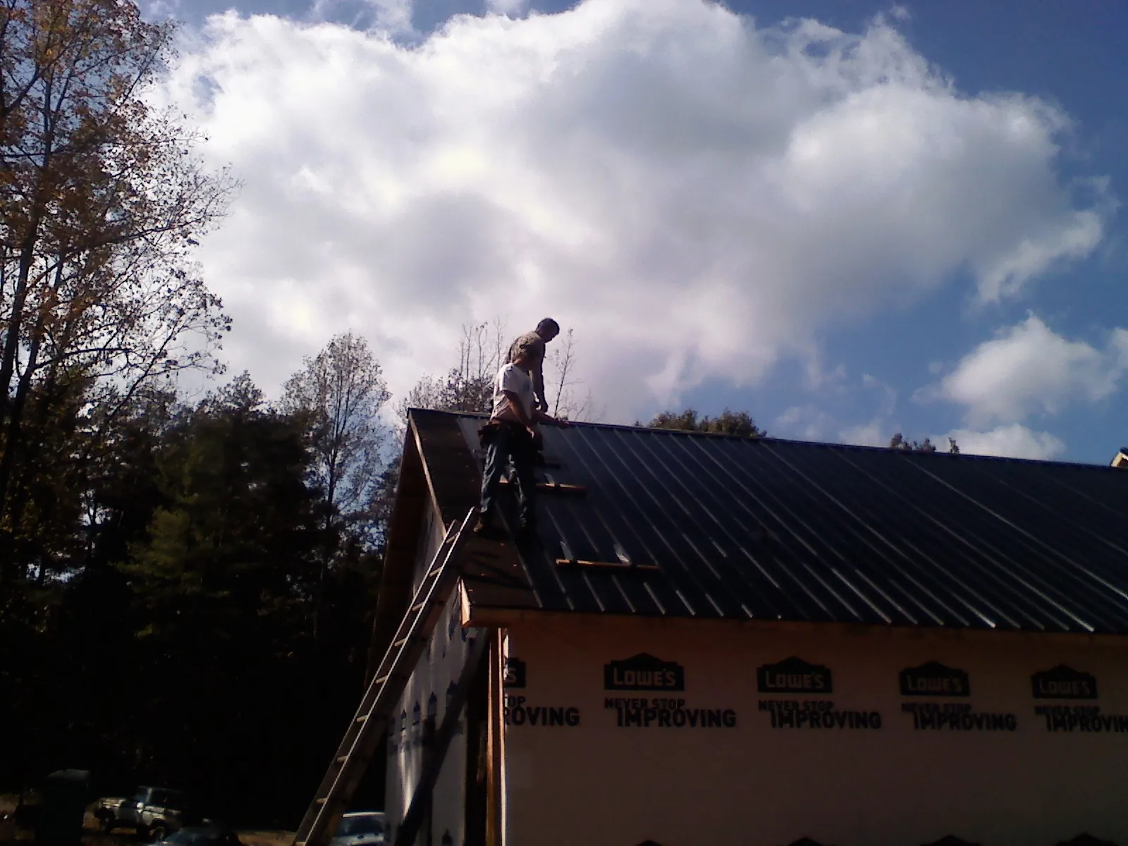 Roofer fastening dark metal panels high against a cloudy sky, from a Roof Inspection job in Park Ridge